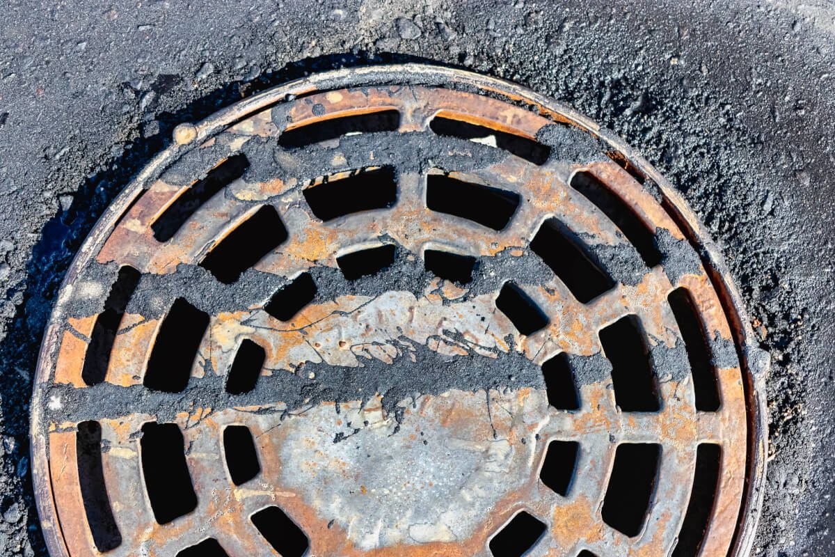 A cast-iron storm sewer hatch on the road before laying the asphalt pavement poured with bitumen. Drainage of rainwater from the road surface. Close-up. manhole with hole forming around it due to soil loss